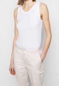 Débardeur blanc en coton lisse, avec de larges bretelles et une coupe ajustée. Associé à un pantalon léger et ample.