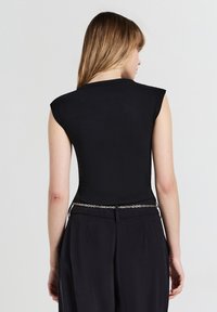 Top nero aderente con maniche a cappuccio, texture liscia e scollo rotondo. Abbinato a pantaloni neri a vita alta e una cintura a catena argentata.