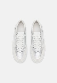 Srebrne metaliczne sneakersy z białymi akcentami z tkaniny, płaskimi sznurówkami, perforowanym detalem na palcach oraz zaokrągloną gumową podeszwą.