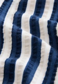 Gestreifter Stoff mit abwechselnden Streifen in Marineblau und Weiß. Die Textur umfasst gerippte und flache Bereiche, die visuelle Tiefe und Kontrast erzeugen.