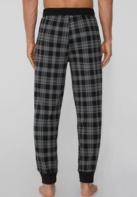 Zwart en grijs geruite loungebroeken met een elastische tailleband en zwarte boorden, gemaakt van zachte stof, met een geblokt patroon.