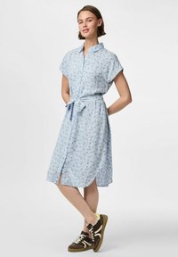 Ljusblå blommig skjortklänning med korta ärmar, knappstängning fram, bälte vid midjan, knälång fåll och sidofickor. Bärs med mörka sneakers.