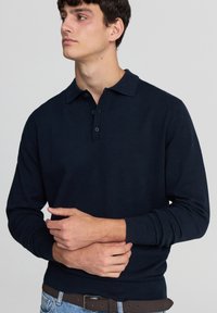 Polo a maniche lunghe blu navy con colletto, patta a tre bottoni e polsini a coste; realizzato in un tessuto morbido e liscio.