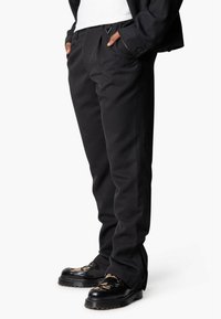 Zwarte op maat gemaakte broeken met een soepele textuur, met een rechte pasvorm en zijzakken, gecombineerd met glanzende zwarte schoenen en gestreepte sokken.