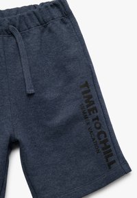 Mørkeblå shorts lavet af blød stof, med en elastisk talje og et trykt slogan "TIME TO CHILL" i sort på siden.