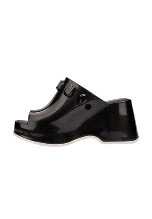 Zuecos de plataforma negros y brillantes con punta abierta, dos acentos decorativos negros y una suela blanca. Textura suave con un acabado brillante.