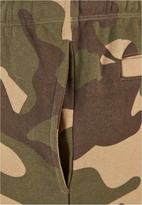 Camo-patterned fabric features shades of green and brown, with a split opening and stitched detailing at the waistband.
