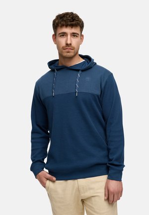 Sudadera azul hecha de tela texturizada con una parte superior de color sólido y una sección inferior acanalada. Cuenta con cordones y detalles del logo en el pecho.