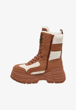 Braune Wildleder-Stiefelette mit weißen Fleece-Akzenten, runder Zehenpartie, dickem strukturiertem Sohlenbereich, Schnürung vorne und seitlichem Reißverschluss für ein einfaches An- und Ausziehen.