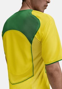 Maglia sportiva gialla con accenti verdi, caratterizzata da una texture a rete, colletto arrotondato e design aderente. Include sezioni perforate per la traspirabilità.