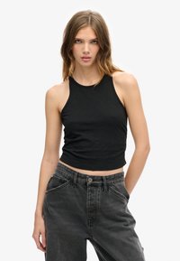 Zwarte mouwloze crop top van zachte stof, met een getailleerd ontwerp en een ronde halslijn, gecombineerd met high-waisted, vervaagde zwarte jeans.
