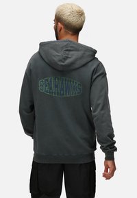 Felpa grigia con una grande grafica "SEAHAWKS" in verde sul retro. Presenta una tasca a marsupio standard e polsini a coste.