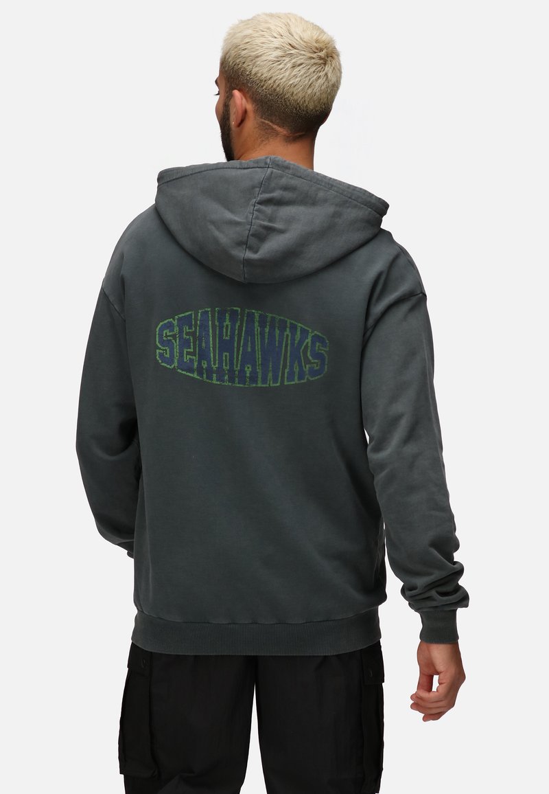 Felpa grigia con una grande grafica "SEAHAWKS" in verde sul retro. Presenta una tasca a marsupio standard e polsini a coste.