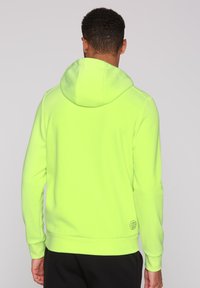 Felpa con cappuccio verde neon, maniche lunghe, tessuto semplice, tasca a marsupio e dettaglio logo vicino all'orlo. Vista posteriore mostrata.