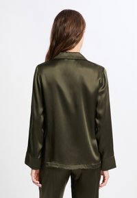 Top de pijama de satén verde oscuro con cuello, mangas largas y una textura lisa. La parte trasera presenta un diseño simple y líneas limpias.