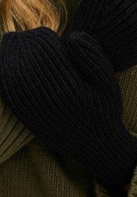 Czarne dziergane rękawiczki z prążkowaną teksturą, noszone z oliwkowozielonym swetrem, ukazujące ciepło i grubość. Skupienie na palcach i okolicy nadgarstka.