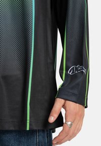 Garās piedurknes melna krekls ar zaļiem akcentiem, ar punktu paraugu, apaļu kakla izgriezumu un logotipa detaļu uz piedurknes.