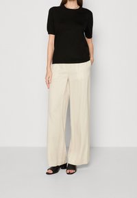 Černý top s krátkým rukávem v kombinaci s krémovými kalhotami širokého střihu. Sandály jsou černé s blokovým podpatkem. Hladká látka a volný střih po celé ploše.