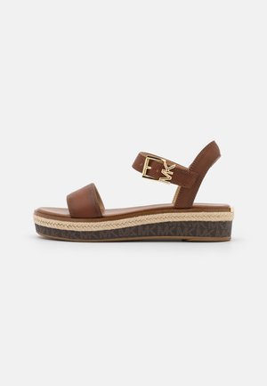 Sandale en cuir marron avec une sangle réglable, quincaillerie dorée et plateforme en espadrille tissée. Présente une semelle extérieure texturée avec logo.