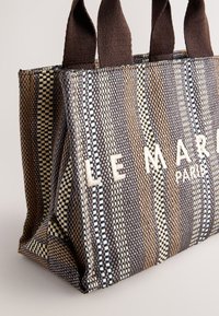 Sac fourre-tout tissé aux nuances de marron, crème et bleu. Comprend un tissu robuste, deux sangles marron et le logo "LE MARAIS PARIS" en blanc.