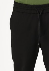 Black jogger pants with an elastic waistband, drawstring, and side pockets. The fabric appears smooth and lightweight.