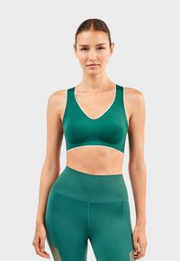 Groene sportbeha met een V-halslijn, contrasterende witte afwerking en een gladde textuur, in combinatie met bijpassende hoog-getailleerde legging.