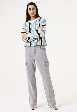 Gebreide trui met een golvend patroon in blauw, beige en zwart. Gecombineerd met grijze cargobroek met zijzakken en een relaxed fit.