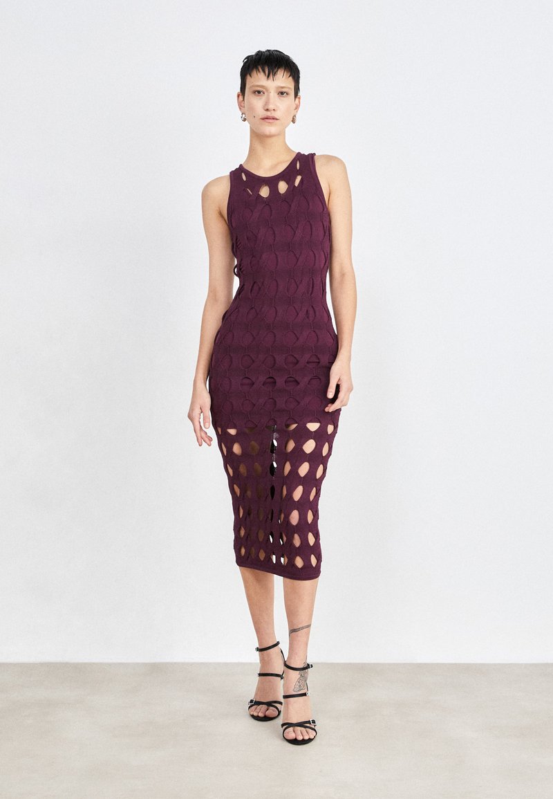 Robe tricotée bourgogne avec découpes ovales, sans manches, longueur mi-mollet et silhouette ajustée, associée à des talons noirs à lanières.