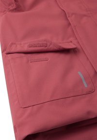 Giacca in tessuto impermeabile rosso con tasca frontale e chiusura in velcro. Presenta un design elegante e un piccolo dettaglio grigio sulla manica.