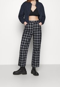 Giacca bomber imbottita navy con chiusura a zip, top corto nero e pantaloni a gamba larga a scacchi bianchi e neri, abbinati a stivali neri chunky.