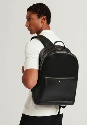 Mochila de cuero negro con forma redondeada, bolsillo frontal con cremallera y correas ajustables; textura suave con patrón sutil de grano.