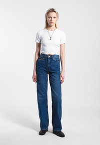 White cropped t-shirt paired with high-waisted blue straight-leg jeans. Model stands on a light background, wearing black shoes.