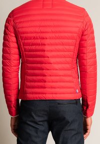 Veste matelassée rouge avec un design matelassé, dotée de manches longues et d'une coupe ajustée. Ornée d'un petit logo en bas à droite.