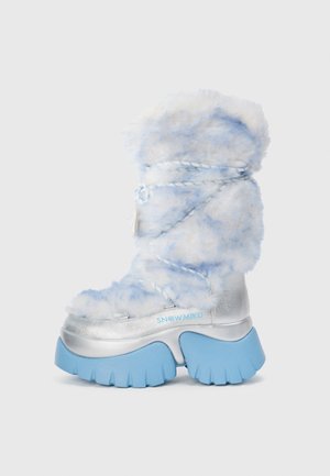 Stivale invernale peloso di colore azzurro chiaro e bianco, con base metallica argentata e suola in gomma blu spessa, caratterizzato da lacci intrecciati e dettaglio del logo.