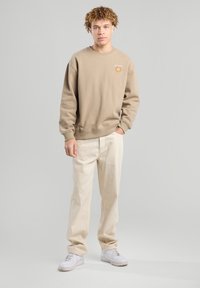 Beige sweatshirt with a round neckline and a California graphic on the chest, paired with cream-colored pants and white sneakers.