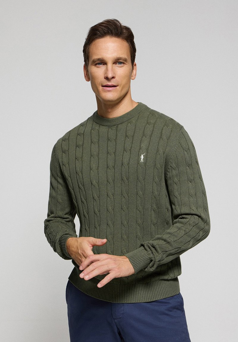 Grön ribbstickad tröja med kabelmönster, rundad halsringning och smala ärmslut. Litet broderat logotyp på bröstet.