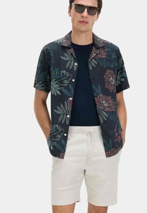 Czarna koszula z krótkim rękawem ozdobiona kolorowymi wzorami kwiatów i liści, zestawiona z beżowymi szortami z troczkami, noszona na granatowej koszulce.