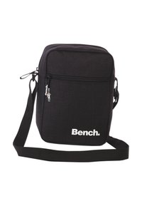 Zwarte schoudertas van stevig materiaal, voorzien van een ritsvak aan de voorkant, verstelbare schouderband en wit logo aan de voorkant.