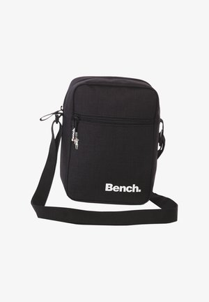 Schwarze Umhängetasche aus strapazierfähigem Gewebe, mit einem Reißverschlussfach auf der Vorderseite, verstellbarem Schultergurt und weißem Logo auf der Vorderseite.