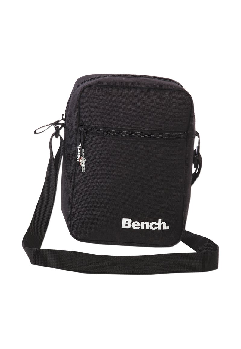 Zwarte schoudertas van stevig materiaal, voorzien van een ritsvak aan de voorkant, verstelbare schouderband en wit logo aan de voorkant.