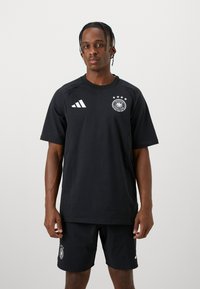 Completo sportivo nero composto da una maglietta a maniche corte con il logo adidas e l'insegna della Germania, abbinato a pantaloni corti coordinati, entrambi in un materiale elegante.