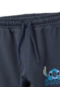 Navyblauwe sweatpants met een elastische tailleband, trekkoord en een lichtblauwe Stitch-figuur graphic aan de voorkant. Zachte textuur.