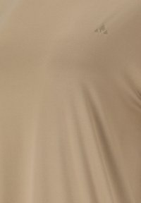 Beiger Stoff mit einem kleinen, dezenten, erhabenen Dreieck-Logo in der oberen rechten Ecke.