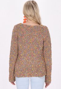 Maglione lavorato a maglia marrone con punti colorati e texture, scollatura ampia, maniche lunghe e una vestibilità leggermente rilassata. Indossato con jeans azzurri.