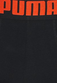 Black shorts with a wide orange elastic waistband featuring the "PUMA" logo in bold letters. Made of stretchable material, smooth texture.