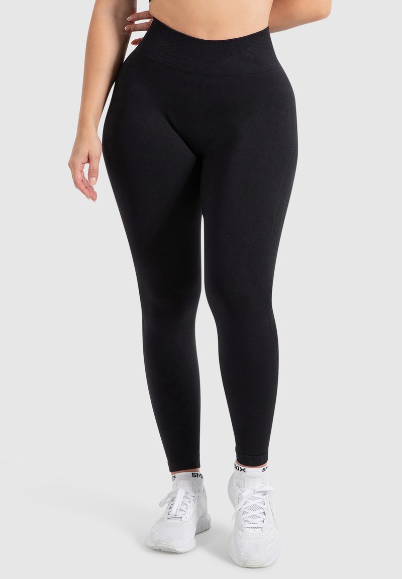 Leggings neri a vita alta, realizzati in tessuto elasticizzato, con una texture liscia e una vestibilità aderente. Abbinati a scarpe athletic bianche.