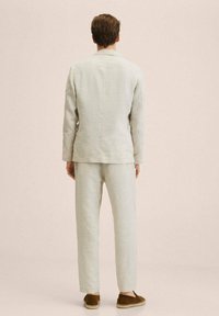 Jasnoszary lniany garnitur z dopasowaną marynarką i luźnymi spodniami. Tkanina ma teksturowane wykończenie. Stylizowany z brązowymi butami wsuwanymi.