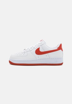 Baskets Nike basses blanches avec le swoosh rouge, languette de talon rouge et semelle rouge, vues de profil sur fond blanc uni.