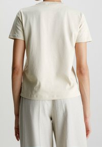 Ljusbeige bomulls T-shirt med korta ärmar, rund halsringning och avslappnad passform, visad bakifrån. Minimala sömnadsdetaljer synliga.