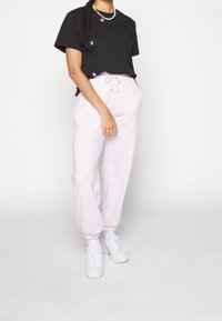 Svart t-shirt med kort ärm och blommiga detaljer, kombinerad med ljusrosa sweatpants med elastisk midja och muddar vid anklarna, bärs med vita sneakers.